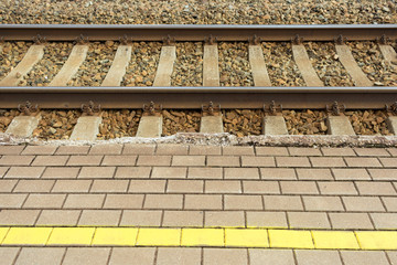 Yellow warning line on cobblestone in front of train tracks.