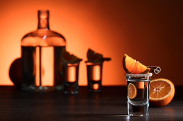 Glasses of tequila with orange and cinnamon sticks on a wooden table.