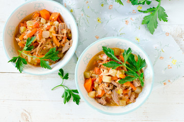 Stew of turkey and vegetables (zucchini, onions, carrots, tomatoes, bell peppers) on a white wooden table