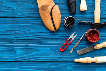 Instruments and materials for make shoes. Shoemaker's work desk. Hummer, awl, knife, sciccors, wooden shoe, insole, paint and leather. Blue wooden background top view copy space