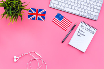 Learn english concept. British and american flags, computer keyboard, notebook for new vocabulary on pink background top view copy space