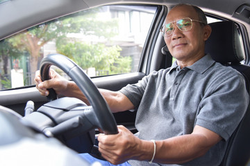 Relaxed Asian Senior man in glasses driving a car.