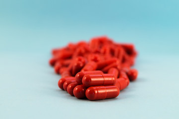 Red capsules with medicine, stacked on a blue background with a focus in the foreground.