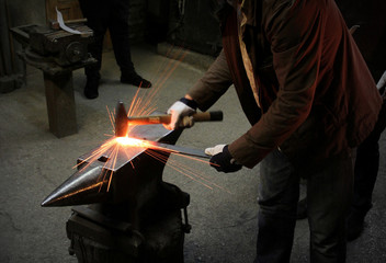 The blacksmith manually forging the molten metal on the anvil in smithy with spark fireworks....