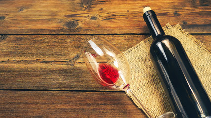 a bottle of wine and a wine glass with red wine on a wooden background.