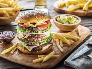 Big hamburger and French fries on the wooden tray.