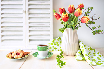 Bunch of red tulips, espresso in green cup with white dots and cookies on light wood