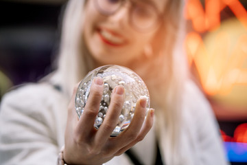 Young girl with glasses and white hair holds a crystal ball.