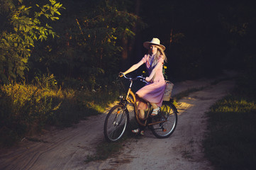 Obraz na płótnie Canvas Beautiful girl wearing a nice pink dress having fun in a park with a bicycle holding a beautiful basket with flowers. Vintage landscapes. Pretty blonde with retro look, bicycle and basket with flowers