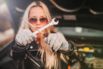 girl beside the open hood of the car with a screwdriver and a key in hand.