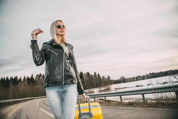 The girl goes on the road with a suitcase, holding a passport with money.