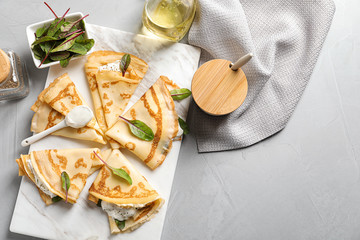 Thin pancakes with sour cream on board, top view