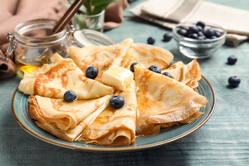 Thin pancakes with honey, berries and butter on plate, closeup