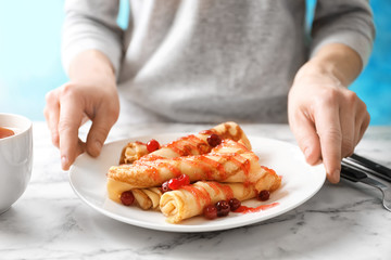 Woman putting plate with thin pancakes, berries and syrup on table