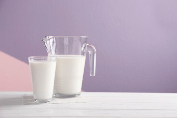 Jug and glass with milk on table against color background