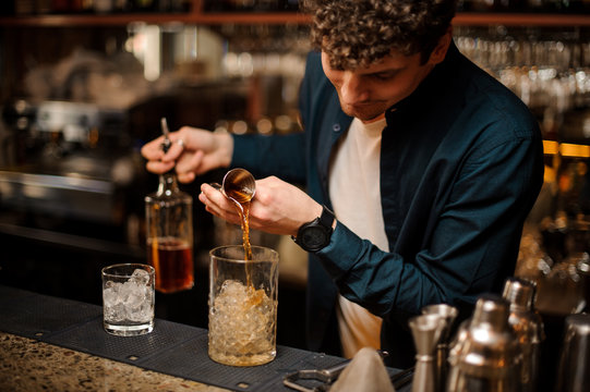 Young barman pouring a sweet syrup into a jar with ice making an alcoholic drink