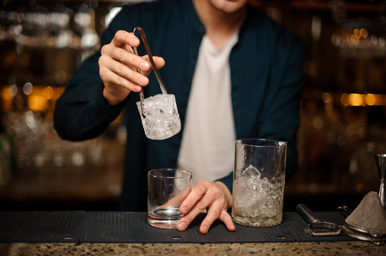 Barman putting a big piece of ice cube into a glass