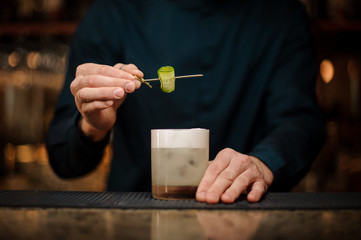 Fototapeta na wymiar Barman decorating a cocktail glass with a cucumber on a wooden skewer