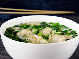 Broth with dumplings in a white bowl. Chinese chopsticks.