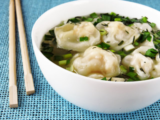 Broth with dumplings in a white bowl. Chinese chopsticks.
