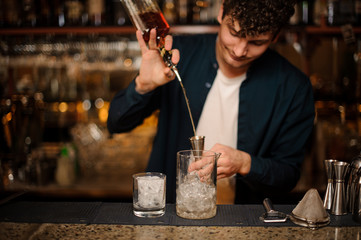 Brunet bartender pouring an alcoholic drink into a measuring cup