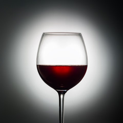 Large glass red wine shape of dark from grapes alcoholic beverage on luminous background advertising shot