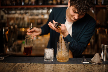 Fototapeta na wymiar Brunet bartender adding an alcoholic drink into a glass with ice
