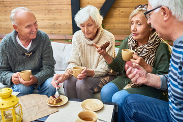 Group of modern seniors enjoying time together drinking tea in outdoor cafe and sharing life...