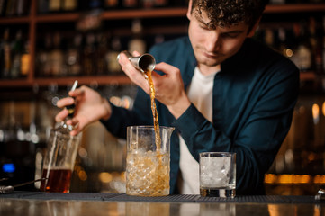 Brunet bartender pouring an alcoholic drink into the glass with ice