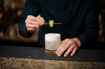 Obraz na płótnie Canvas Bartender serving a cocktail with a cucumber at bar counter