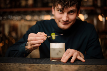 Smiling bartender serving a cocktail with a cucumber at bar counter