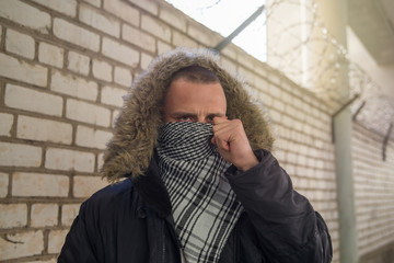young guy with Arabian appearance covers his face keffiyeh near the brick wall with barbed wire....