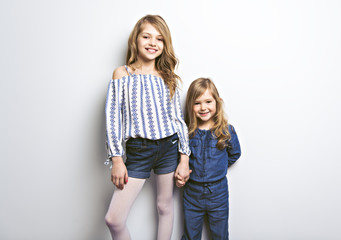Joyful beautiful child with her sister close to a white wall