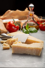 Traditional italian food - aged Italian parmesan hard cheese Parmigiano-Reggiano with cheese knife, tomato, basil, olive oil