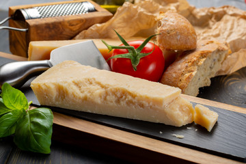 Traditional italian food - aged Italian parmesan hard cheese Parmigiano-Reggiano with cheese knife, tomato, basil, olive oil