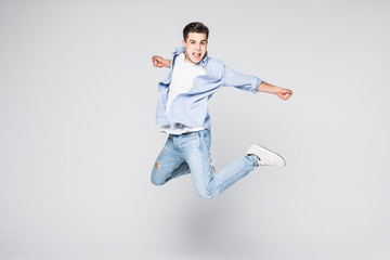 Full-length photo of funny man in casual t-shirt and jeans running or jumping in air isolated over...