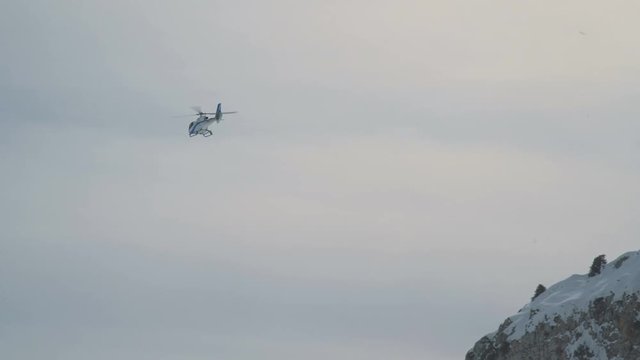 The helicopter flies against the background of a rocky snow-capped mountain