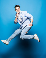 Happy excited cheerful young man jumping and celebrating success isolated on blue background