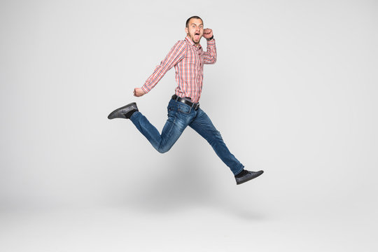 Vertical image of happy man in shirt and jeans which jumping in studio over white background
