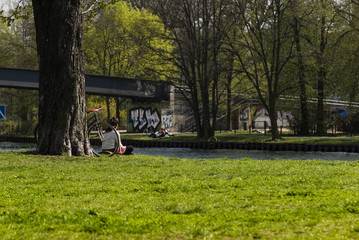 Parkwiese im Frühling, Frau sitzt auf einer Wiese am Wasser, frische grüne Parkwiese,...