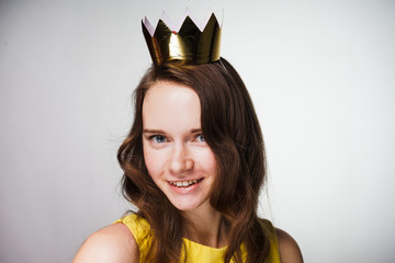 beautiful young woman in a yellow dress looks at the camera and smiles, on her head a golden crown