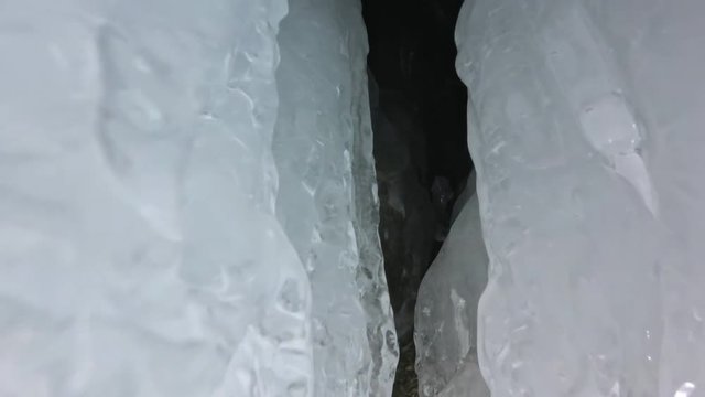 Travel woman on ice cave of Lake Baikal. Pov view selfie. Girl backpacker is walking of ice grot. Traveler looks at beautiful ice grotto. Hiker wears sports glasses, silver jacket, backpack, led lamp