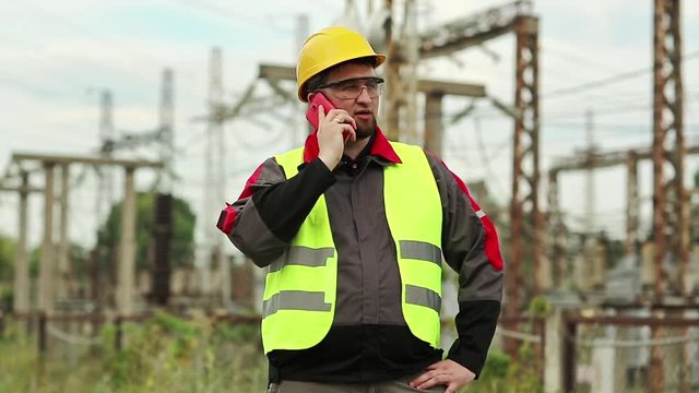 Worker on electric power plant speaks on smartphone. Power engineering specialist with cell phone on electric power station