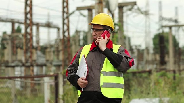 Worker on electric power plant speaks on smartphone. Power engineering specialist with cell phone on electric power station