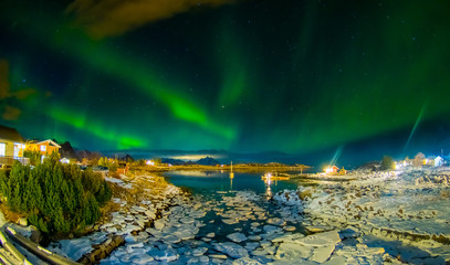 Amazing outdoor view of green aurora borealis in the sky during night and small and medium pieces of Ice left behind during a low tide on a frozen lake