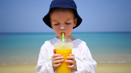 boy of two years drinking mango fresh on the beach on the background of the ocean.