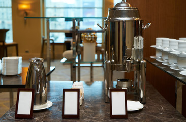 Hot water pot and coffee kettle with empty cards for text on serving table in restaurant
