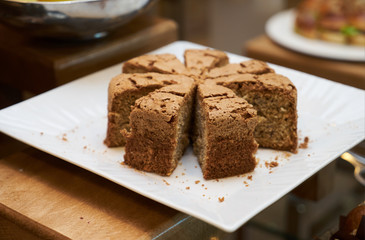 Delicious sponge cake pieces with walnuts on a white cake board on wooden table, close-up
