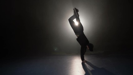 Freestyle dance male teacher performing break dancing tricks in slow motion in a foggy room