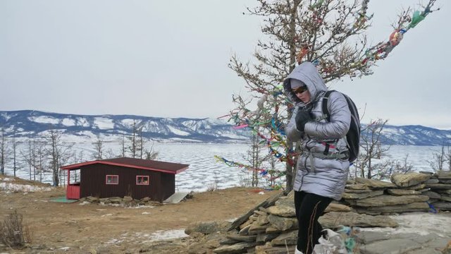 Travel of woman on ice of Lake Baikal. Close unique buddhist stupa burkhan monument symbol mystical historic ritual island Ogoi landscape mountains shamanic worship. Trip to winter island. Hiker wears